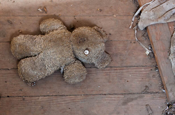 A one-eyed teddy bear left on the floor in an abandoned farmhouse